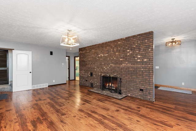 unfurnished living room with dark hardwood / wood-style floors, a textured ceiling, a chandelier, and a brick fireplace