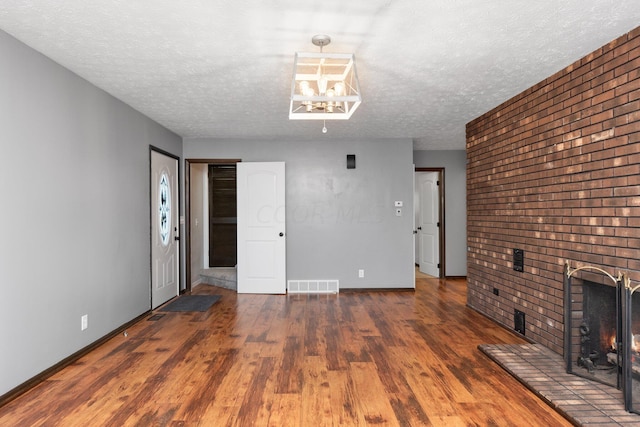 unfurnished living room featuring a textured ceiling, dark hardwood / wood-style floors, and a brick fireplace