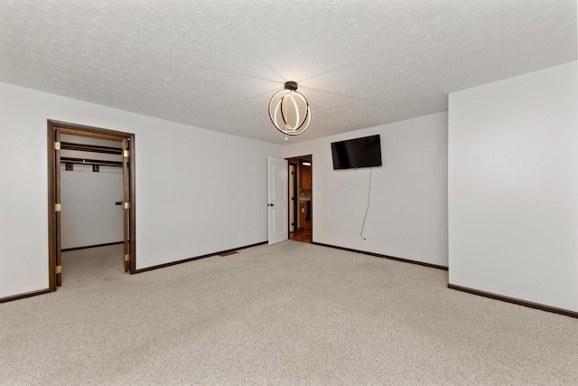 unfurnished bedroom featuring a spacious closet, a closet, light colored carpet, and a textured ceiling