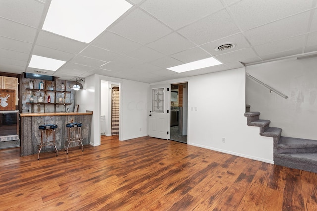 basement featuring bar, a drop ceiling, and dark hardwood / wood-style floors