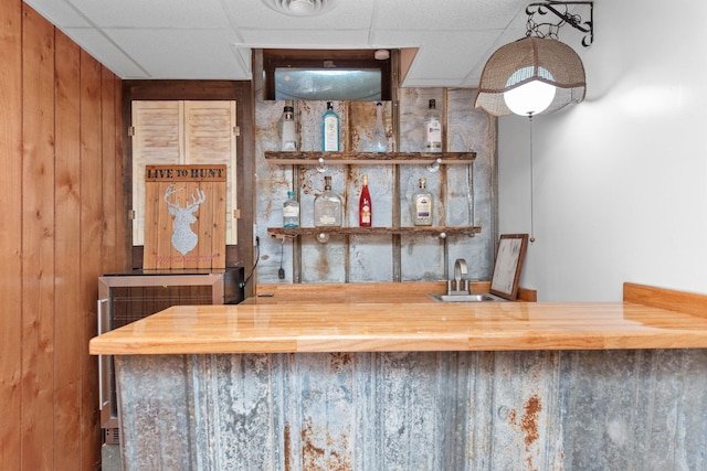 bar featuring butcher block countertops, wooden walls, a drop ceiling, and sink