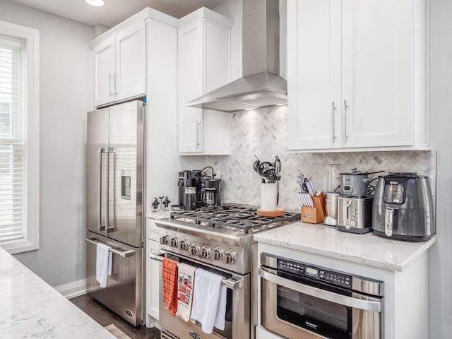 kitchen featuring light stone countertops, white cabinetry, high quality appliances, and wall chimney range hood