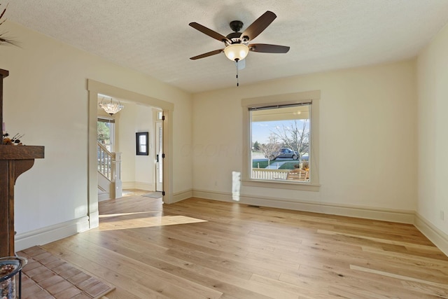 spare room featuring ceiling fan with notable chandelier, a textured ceiling, and light hardwood / wood-style flooring