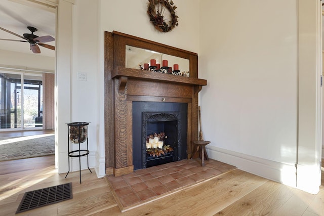 details with ceiling fan, wood-type flooring, and a tiled fireplace