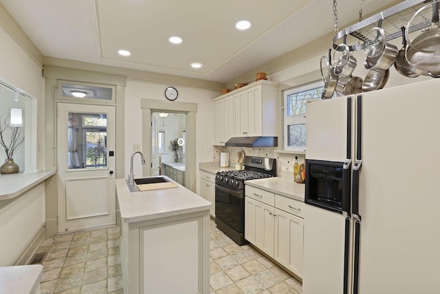 kitchen featuring stainless steel gas stove, plenty of natural light, white fridge with ice dispenser, and a center island with sink