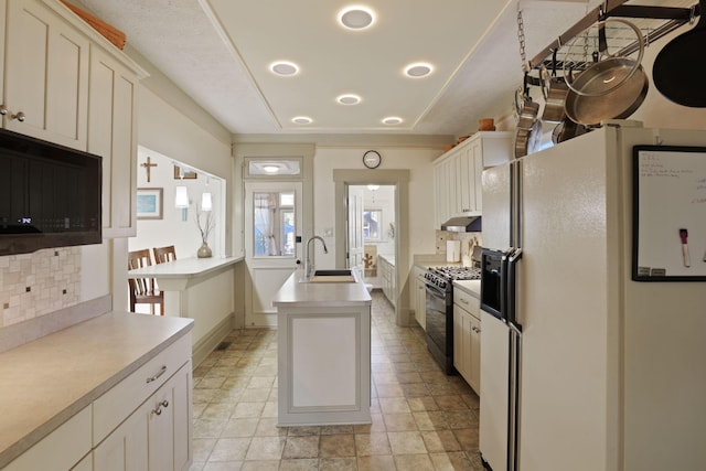 kitchen with backsplash, gas stove, sink, white refrigerator with ice dispenser, and a kitchen island