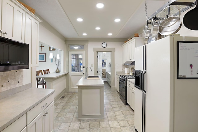 kitchen featuring tasteful backsplash, black range with gas stovetop, white cabinetry, white fridge with ice dispenser, and an island with sink