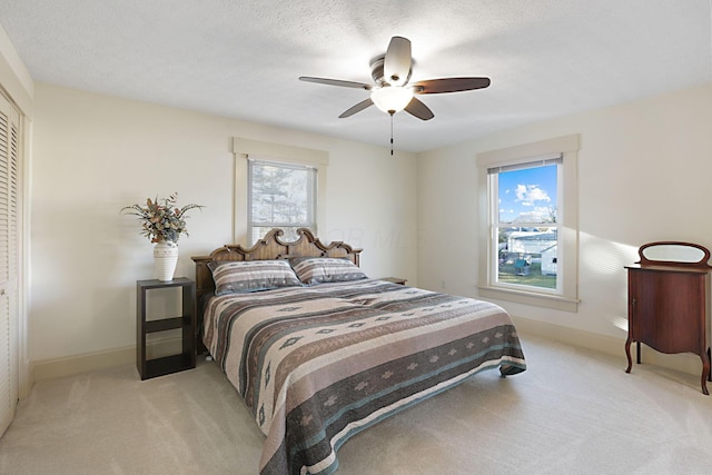 bedroom with ceiling fan, light colored carpet, a textured ceiling, and a closet