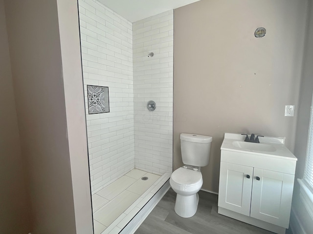 bathroom featuring toilet, vanity, wood-type flooring, and tiled shower