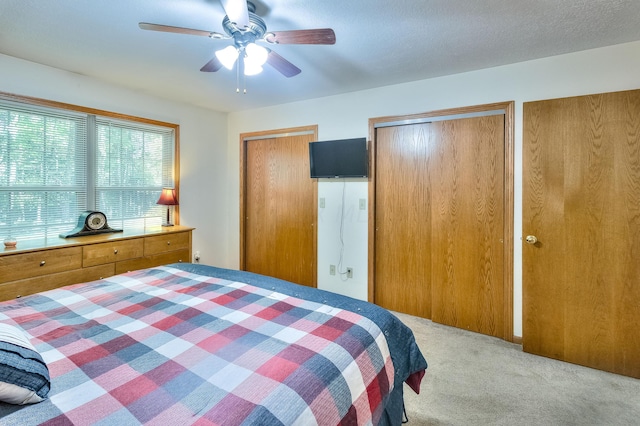 carpeted bedroom with multiple closets, ceiling fan, and a textured ceiling