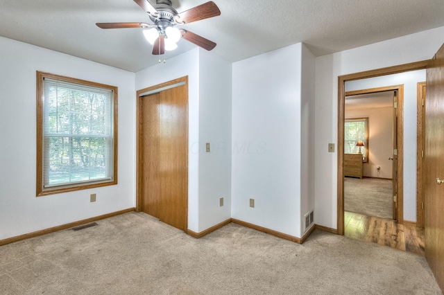 unfurnished bedroom with a textured ceiling, ceiling fan, light carpet, and a closet