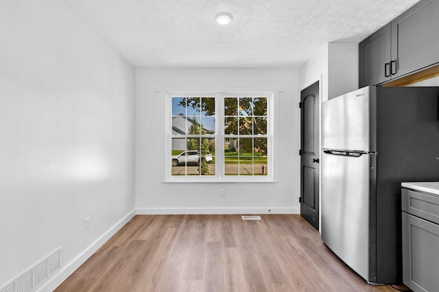 kitchen with stainless steel refrigerator, gray cabinets, light hardwood / wood-style floors, and a textured ceiling