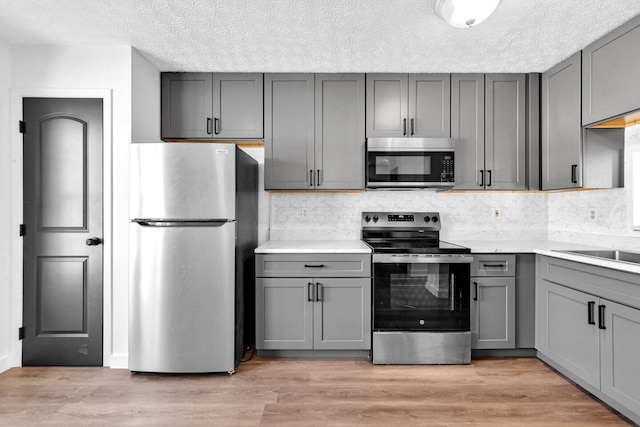 kitchen featuring gray cabinetry, a textured ceiling, tasteful backsplash, light hardwood / wood-style floors, and stainless steel appliances