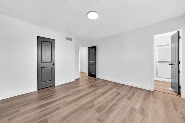 unfurnished bedroom featuring light wood-type flooring, a textured ceiling, and connected bathroom