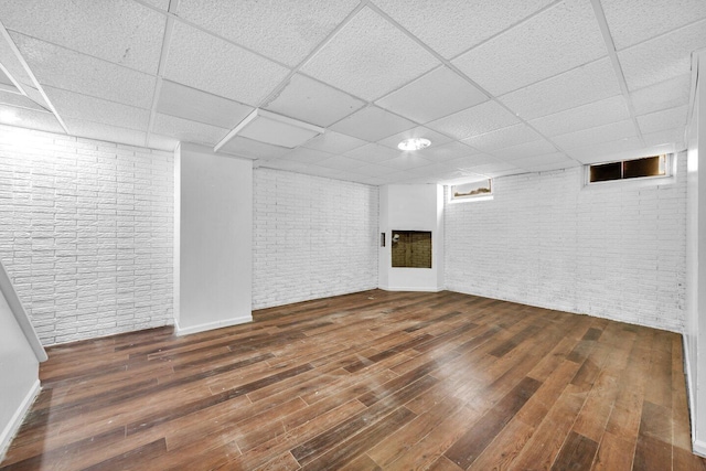 basement featuring a paneled ceiling, brick wall, and dark hardwood / wood-style floors