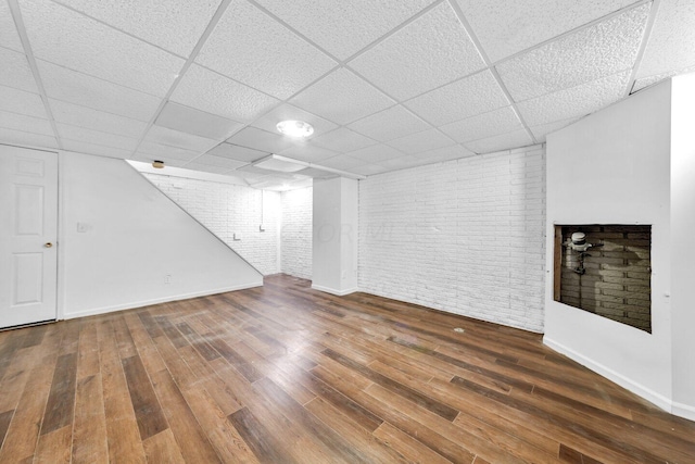 basement featuring a paneled ceiling, hardwood / wood-style flooring, and brick wall