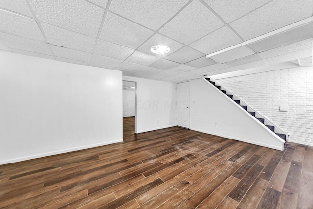 basement featuring a paneled ceiling, dark hardwood / wood-style floors, and brick wall