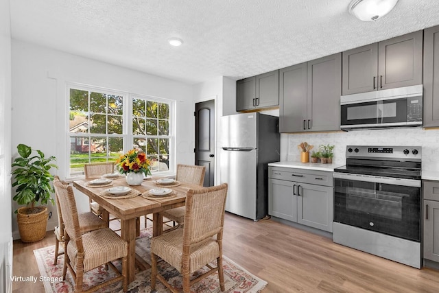 kitchen with backsplash, gray cabinets, light wood-type flooring, a textured ceiling, and appliances with stainless steel finishes