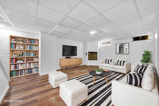 living room with wood-type flooring, a paneled ceiling, and brick wall