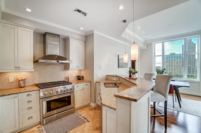 kitchen with light stone countertops, stainless steel range, a breakfast bar, sink, and wall chimney range hood