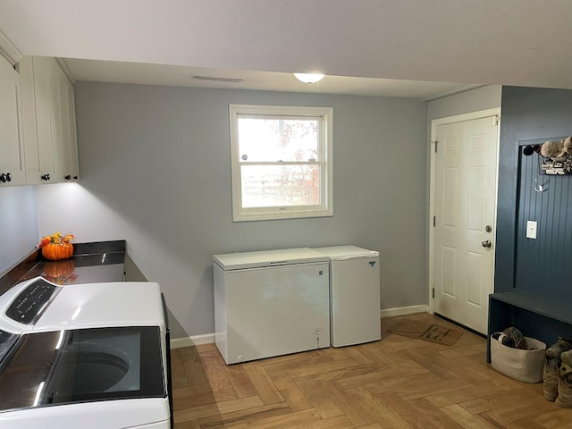 clothes washing area featuring separate washer and dryer, light parquet flooring, and cabinets