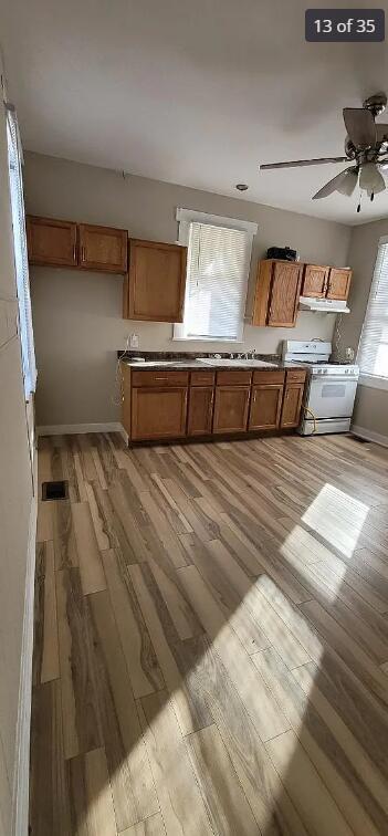 kitchen featuring white range with gas cooktop, ceiling fan, light hardwood / wood-style flooring, and a healthy amount of sunlight