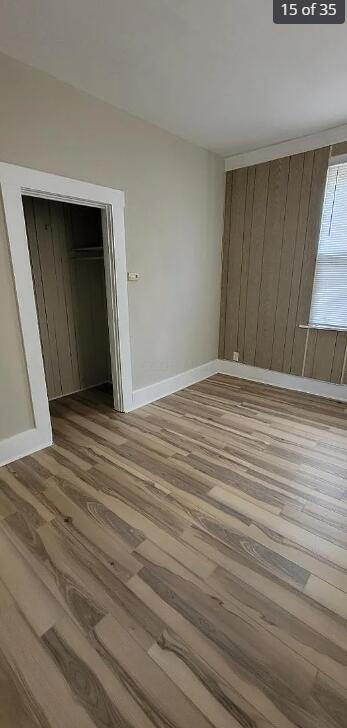 unfurnished bedroom featuring wood-type flooring, a closet, and wooden walls