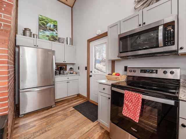 kitchen featuring light stone counters, stainless steel appliances, vaulted ceiling, and light wood-type flooring