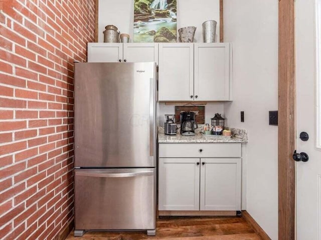 kitchen featuring light stone counters, brick wall, dark hardwood / wood-style floors, white cabinetry, and stainless steel refrigerator