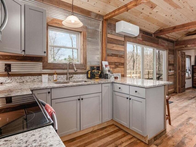 kitchen with sink, light stone counters, a wall unit AC, light hardwood / wood-style floors, and decorative light fixtures