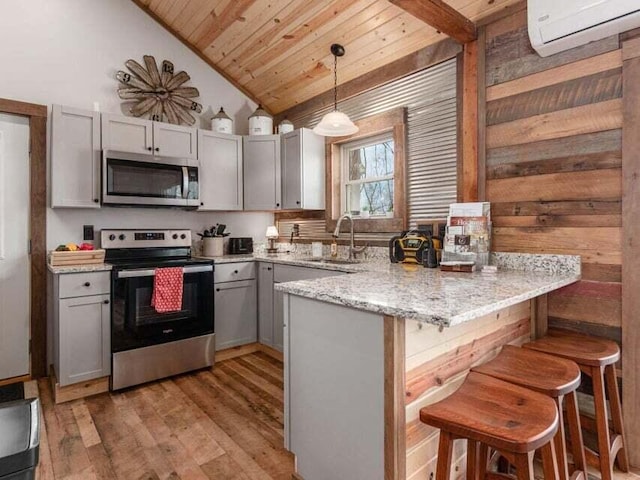 kitchen featuring kitchen peninsula, appliances with stainless steel finishes, a wall mounted air conditioner, light hardwood / wood-style flooring, and hanging light fixtures