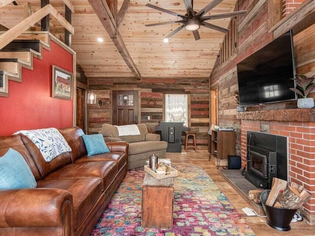 living room featuring a wood stove, wooden walls, hardwood / wood-style flooring, vaulted ceiling with beams, and ceiling fan