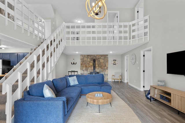 living room featuring wood-type flooring, a wood stove, a towering ceiling, and a chandelier