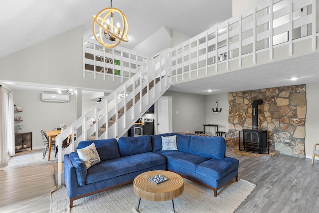 living room with a wall mounted AC, hardwood / wood-style flooring, high vaulted ceiling, a chandelier, and a wood stove