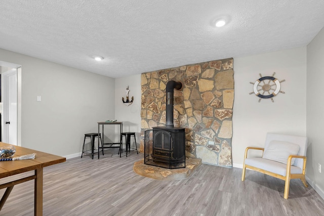 living area featuring a wood stove, light hardwood / wood-style floors, and a textured ceiling