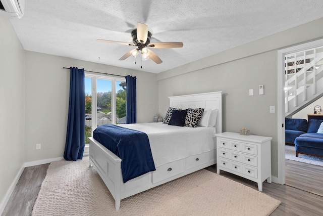 bedroom with a textured ceiling, ceiling fan, a wall mounted air conditioner, and light wood-type flooring