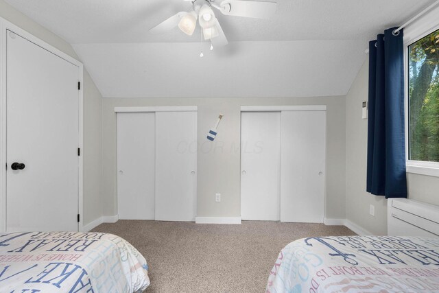 carpeted bedroom featuring ceiling fan, multiple closets, a textured ceiling, and vaulted ceiling