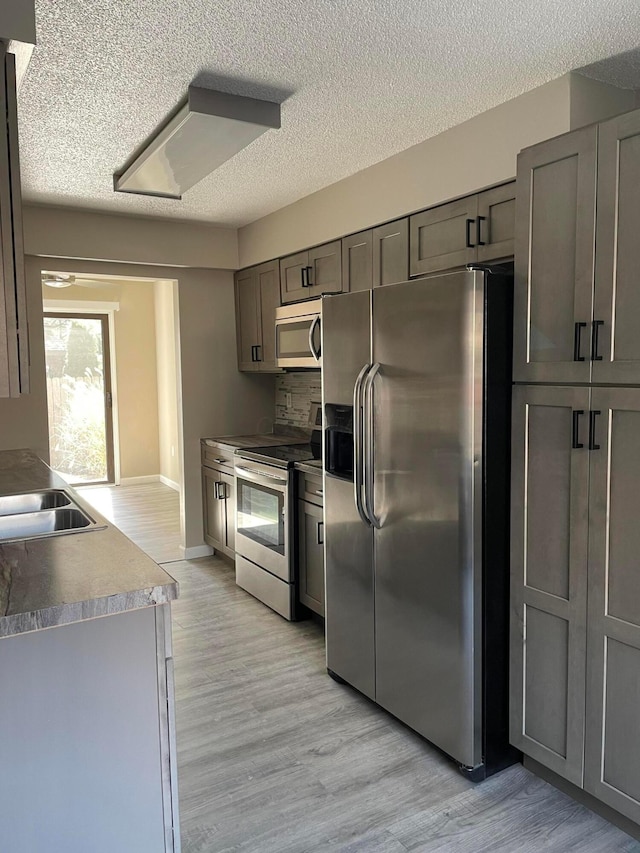 kitchen with appliances with stainless steel finishes, sink, a textured ceiling, and light hardwood / wood-style flooring