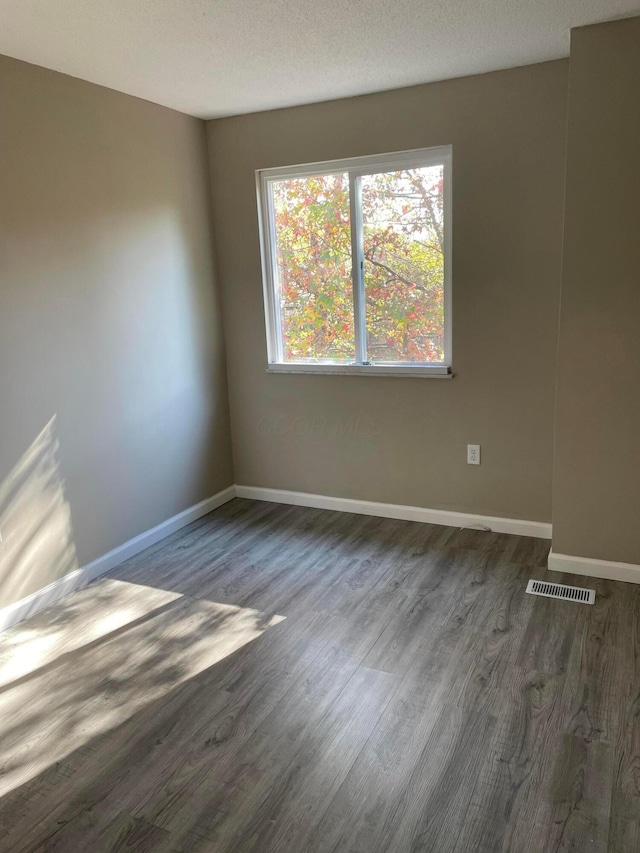 spare room featuring dark wood-type flooring and a textured ceiling