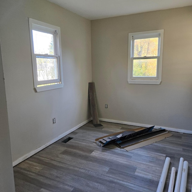 empty room with baseboards, wood finished floors, visible vents, and a healthy amount of sunlight