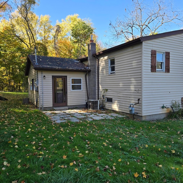 back of house with a chimney, cooling unit, and a lawn