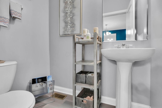 bathroom with hardwood / wood-style floors, an inviting chandelier, and toilet