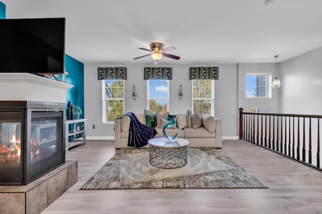 living room featuring hardwood / wood-style flooring, ceiling fan with notable chandelier, and a multi sided fireplace