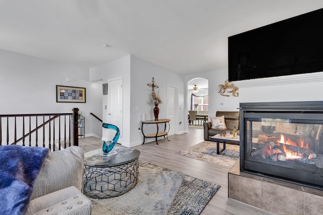 living room with a multi sided fireplace, light wood-type flooring, and ceiling fan