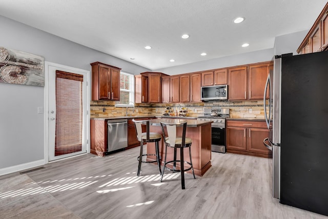 kitchen with stainless steel appliances, tasteful backsplash, a breakfast bar area, a kitchen island, and light wood-type flooring