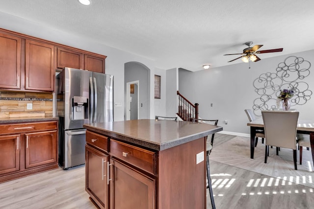 kitchen with decorative backsplash, stainless steel fridge, light wood-type flooring, ceiling fan, and a kitchen island