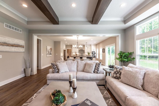 living room with beamed ceiling, a notable chandelier, ornamental molding, and dark wood-type flooring