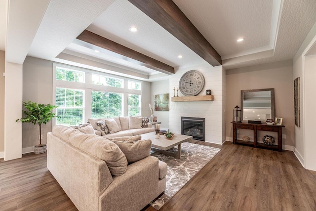 living room with beamed ceiling, dark hardwood / wood-style flooring, a large fireplace, and a tray ceiling