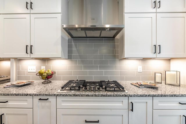 kitchen featuring white cabinets, tasteful backsplash, stainless steel gas cooktop, and wall chimney exhaust hood