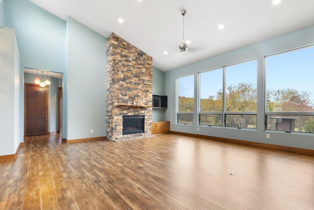 unfurnished living room with a stone fireplace, high vaulted ceiling, wood-type flooring, and a notable chandelier